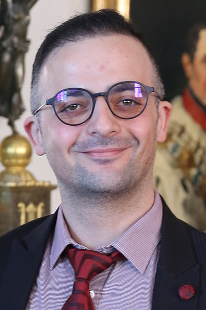 A man with glasses looks into the camera with a smile.