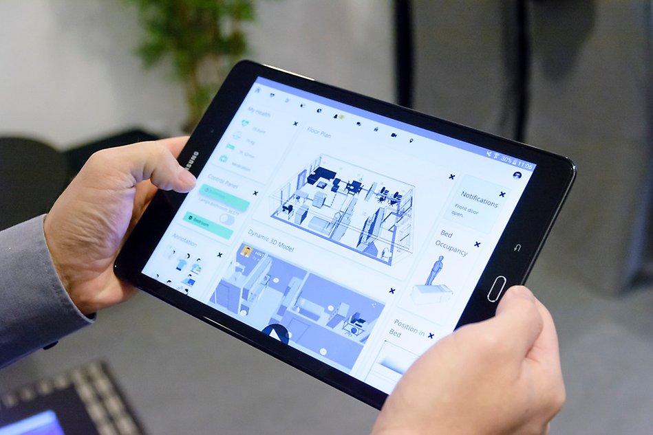  Two hands holding a tablet showing floor plan over an apartment. Photo.
