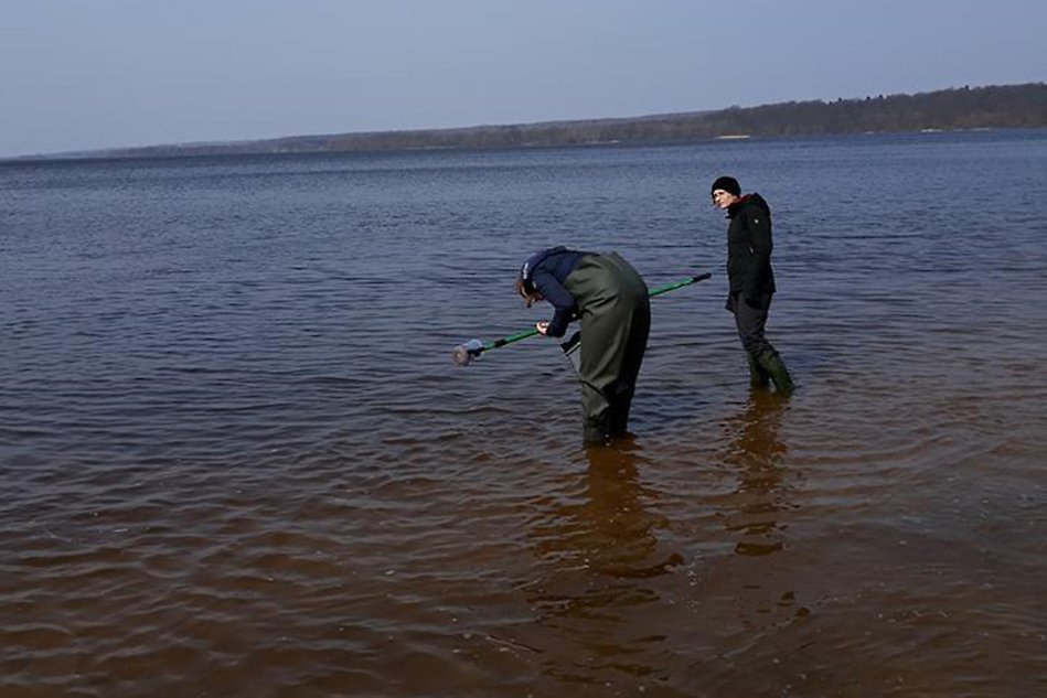 Two people standing in water taking samples. Photo.