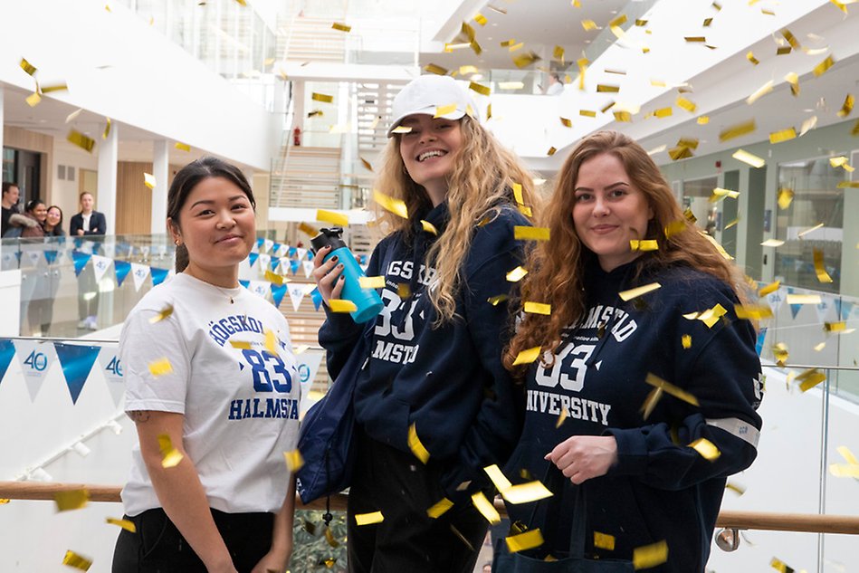 Tre kvinnor iklädda profilprodukter bakom fallande konfetti. Foto. 