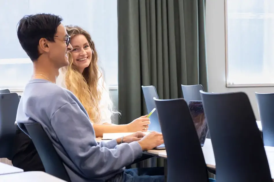 En leende kvinna håller en surfplatta och visar den för en man som står bredvid. Foto.