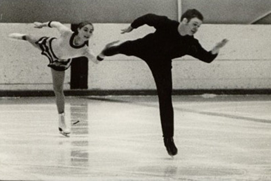 A pair of figure skaters in competition attire on the ice. Black and white photo.