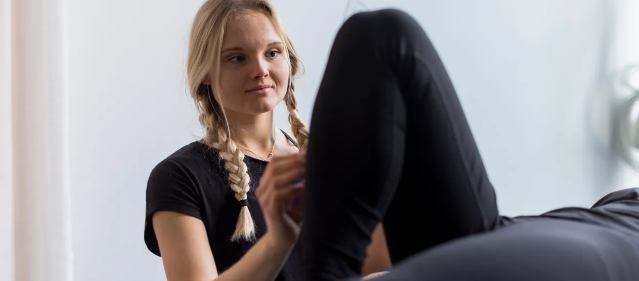 A young woman is examining a leg on a person lying down. Photo.