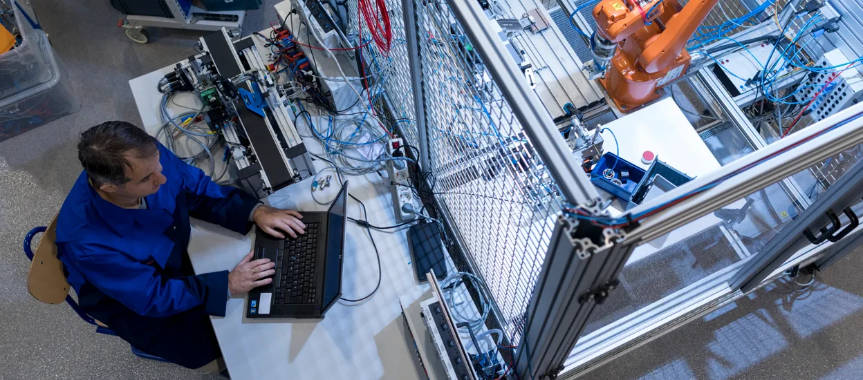 Aerial view of a robotic arm and a man sitting at a computer. Photo.