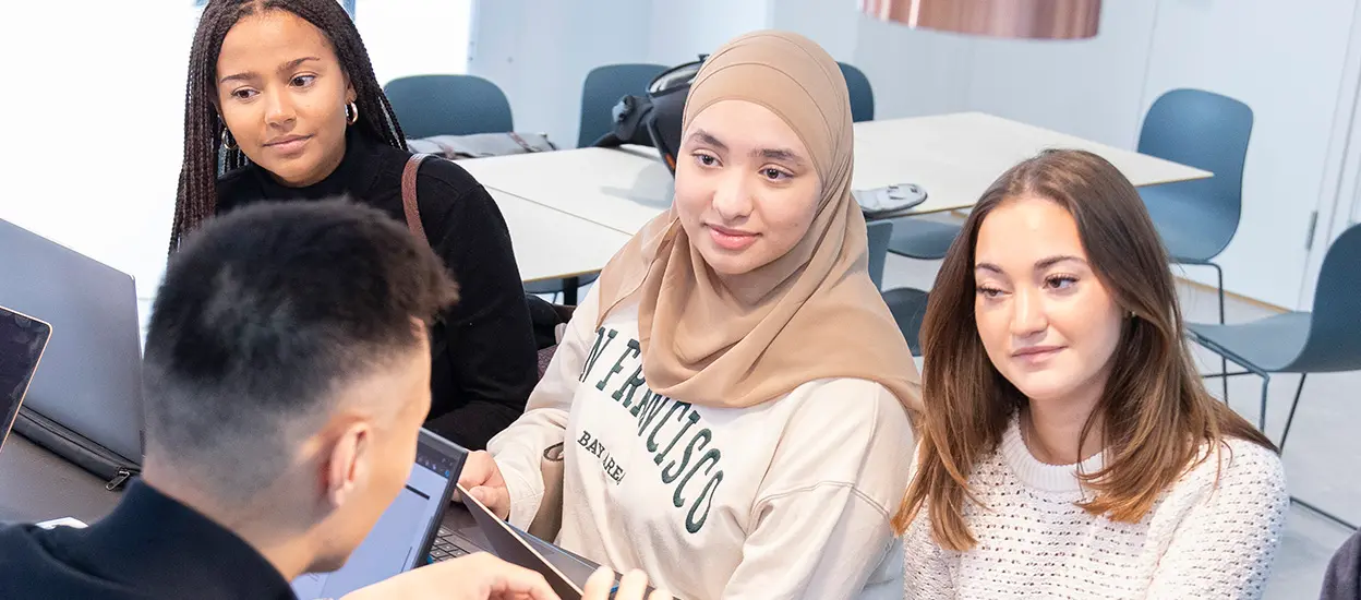 Fyra studenter sitter och diskuterar i en lärosal. Tre kvinnor är vända mot kameran. En man sitter med ryggen mot kameran. Foto.