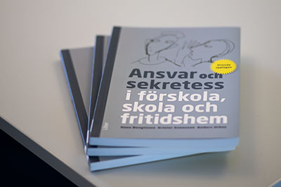 Tre böcker ligger i solfjädersform på en vit skolbänk.
