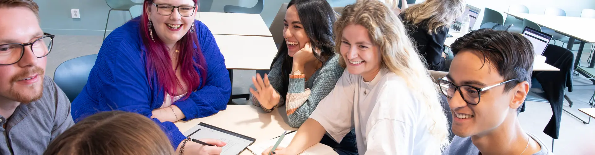 A group of young people sit at a table and smile at each other. Photo.