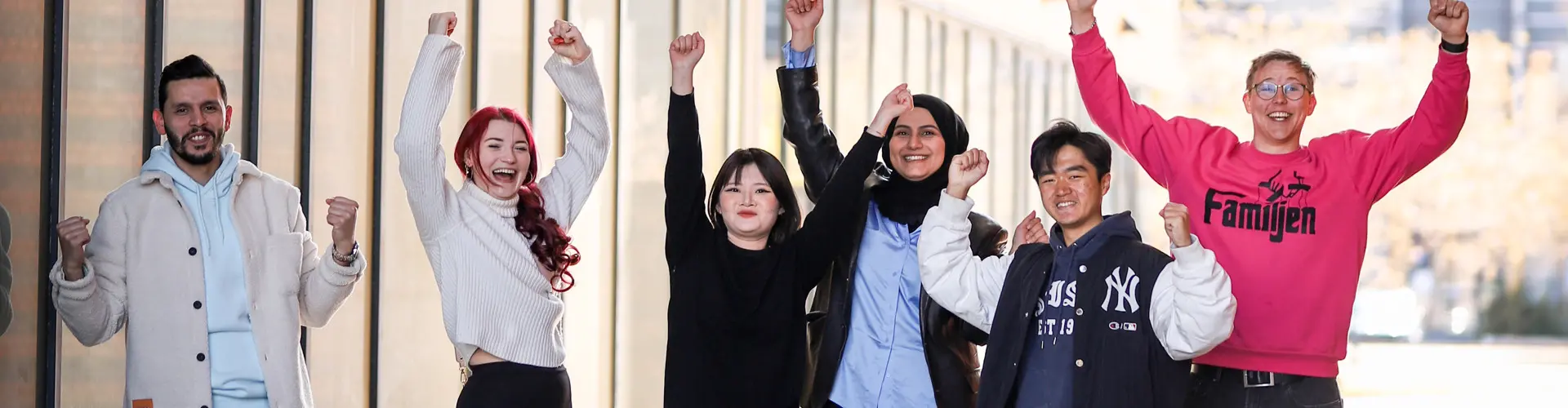 Six smiling people stand in a row and raise their arms in the air. Photo.