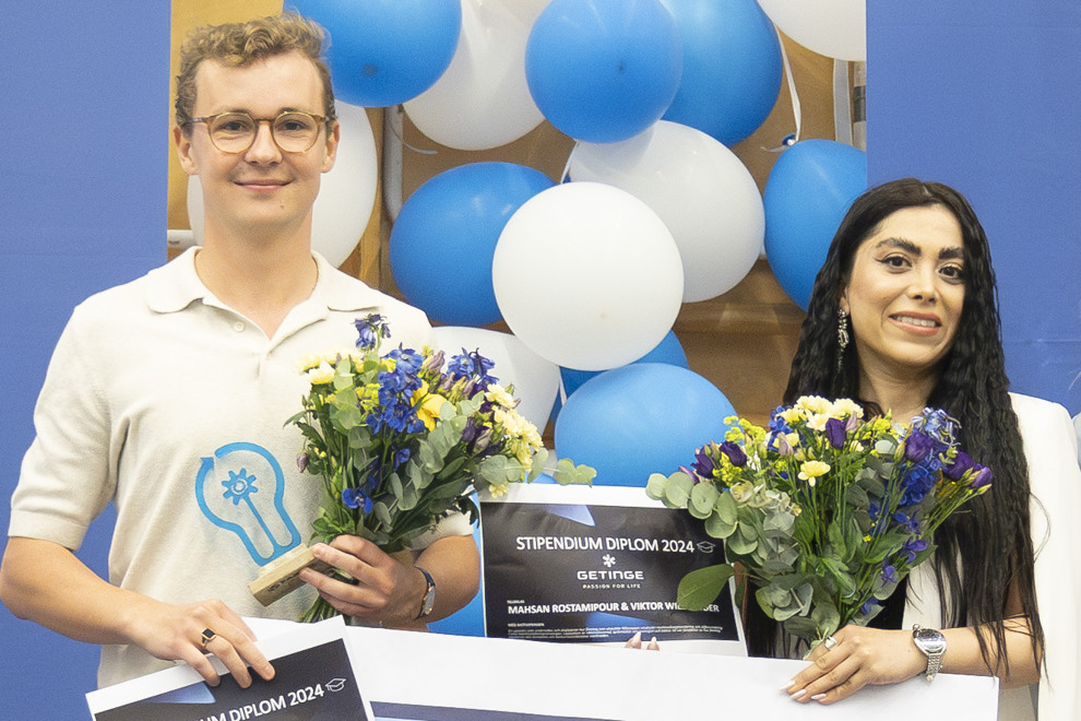 Två studenter håller i en varsin blombukett, statyett och check. Foto.