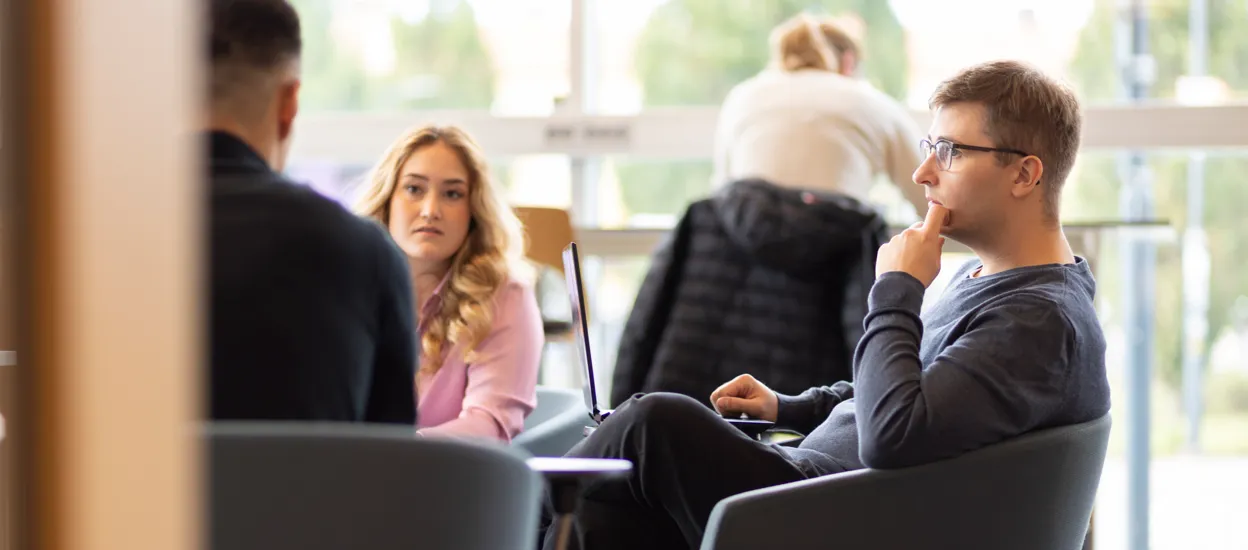 Studenter sitter i fåtöljer i ett bibliotek och diskuterar med varandra. Foto.