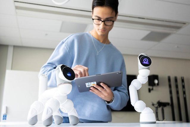 En manlig student håller i en läsplatta och tittar på en robothund