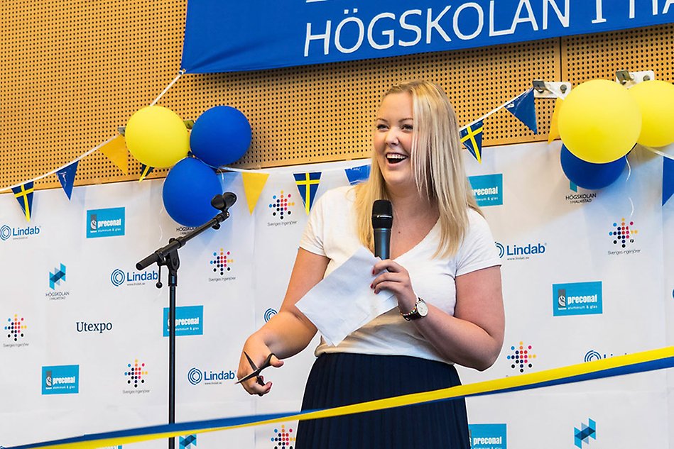 Invigningstalare står med en sax på scenen redo att klippa bandet.