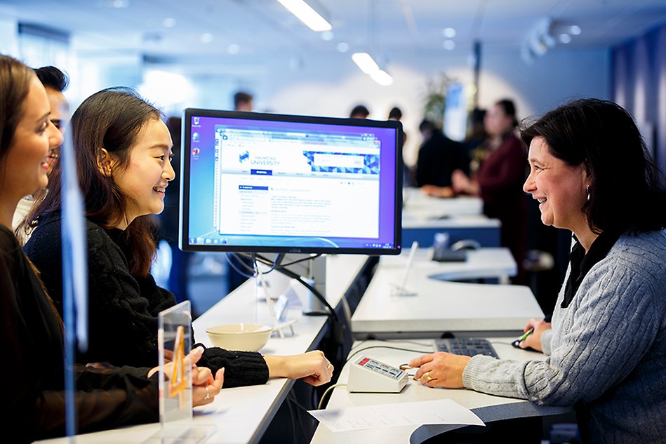 Kvinna vid en servicedesk visas två andra personer information på en datorskärm. Foto.