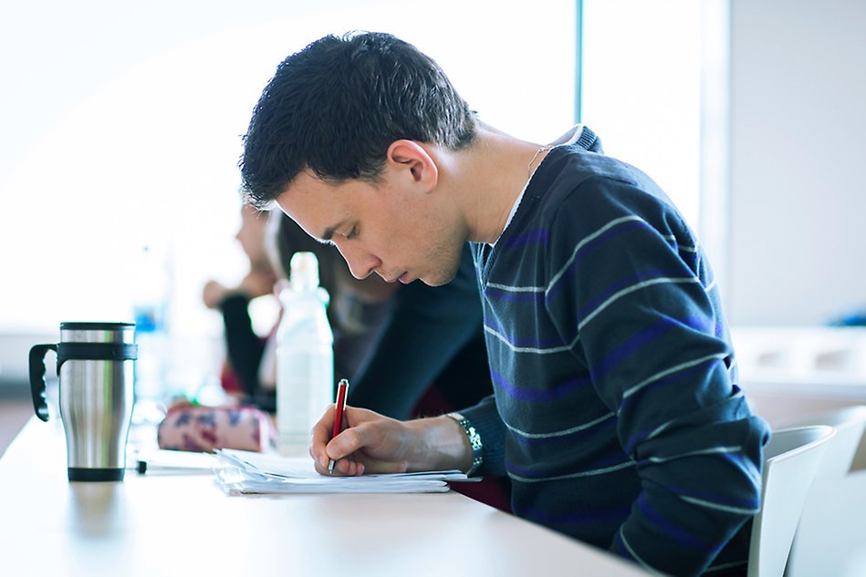 Manlig student som sitter och skriver tenta, bilden är tagen i profil. Foto.
