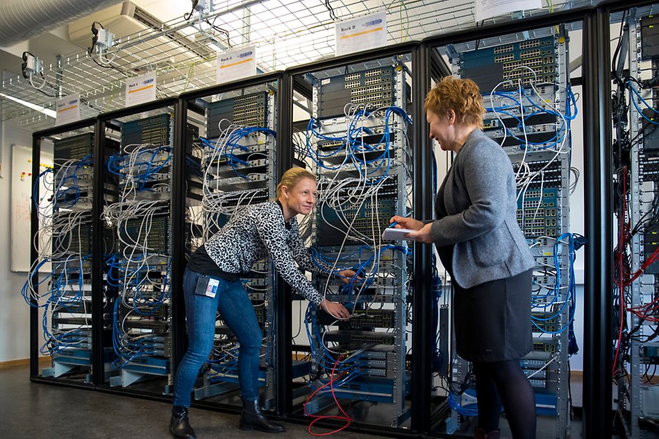 Två kvinnor visar sladdar och datorer vid en server. Foto.