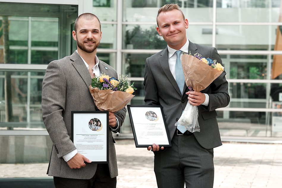 Two people in suits are holding Forterro scholarship diplomas and flowers.