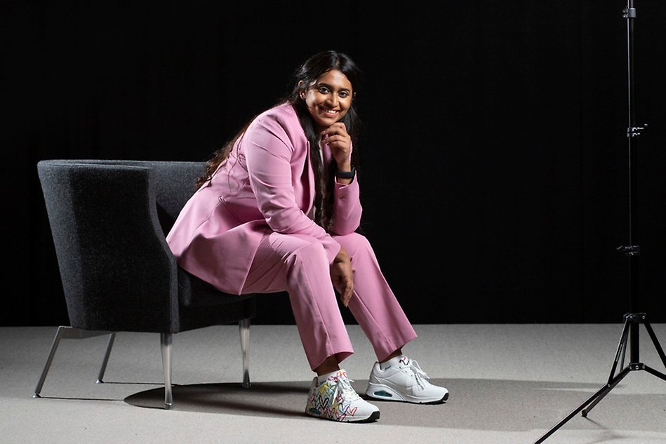 A woman in a pink suit is sitting on a chair looking into the camera. Photo. 