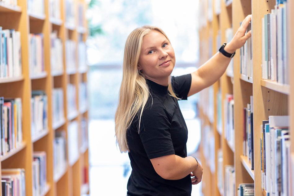 A person with blonde hair in the middle of book shelves. Photo.