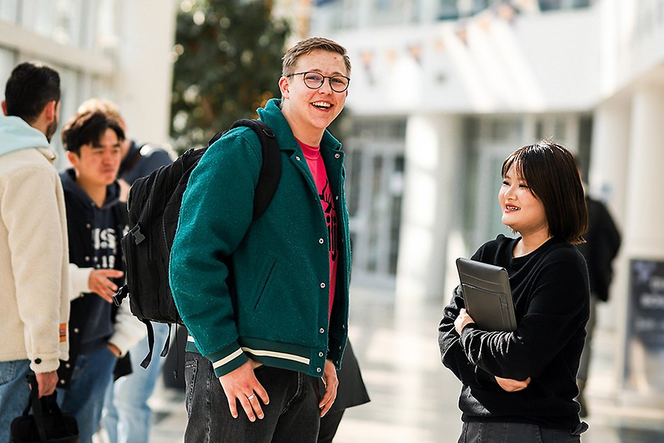 A young man and young woman talking in a hall at campus. Photo.