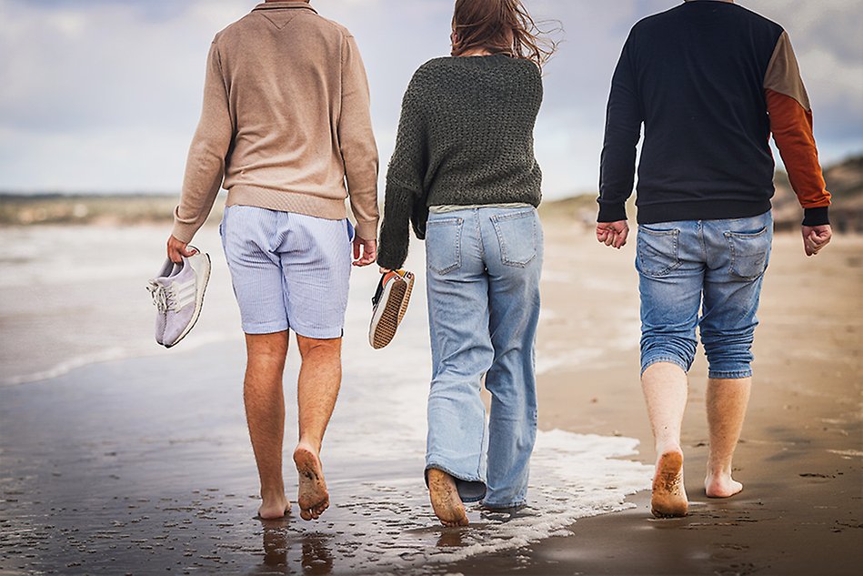 Three students walking barefoot on the beach with their backs towards the camera. Photo.