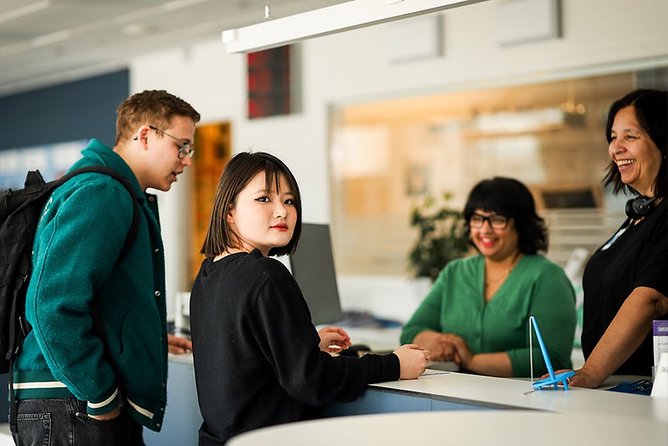 Two students are talking to two persons behind a reception desk. photo.