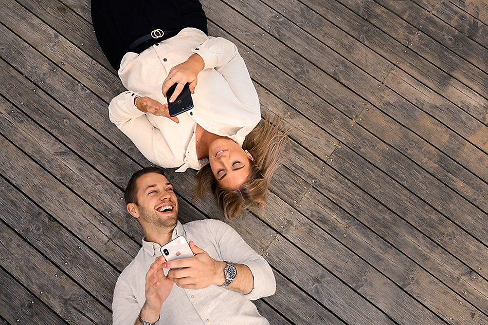 A male and a female lying on a wooden floor with their mobile phones in their hands. Photo.