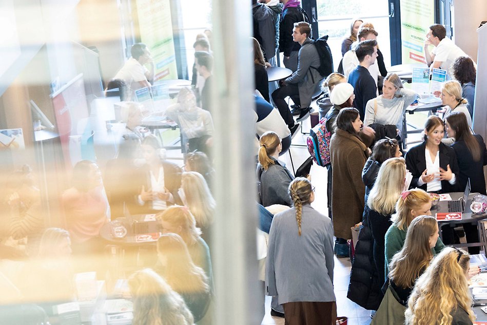 Studenter pratar med utställare utanför en föreläsningssal. Spegelbild. Foto.