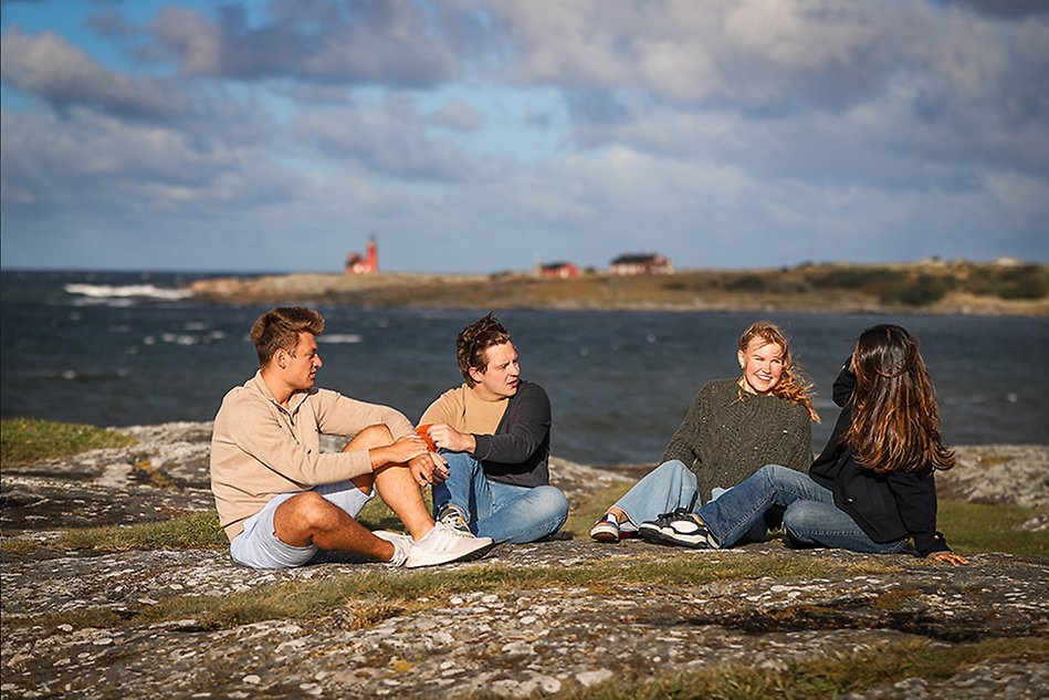 A group of students witting on a cliff by the beach. Photo.