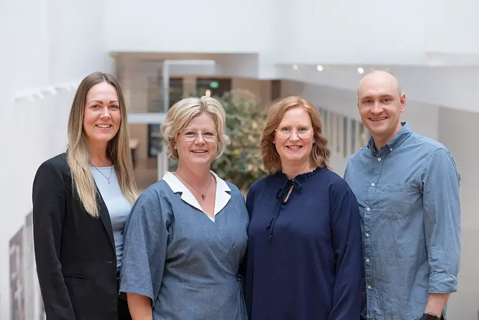 Four people are smiling and looking into the camera. Photo.