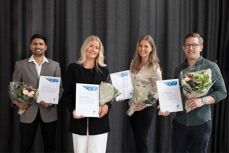 Fyra leende personer står bredvid varandra, alla håller var sitt diplom och blommor.