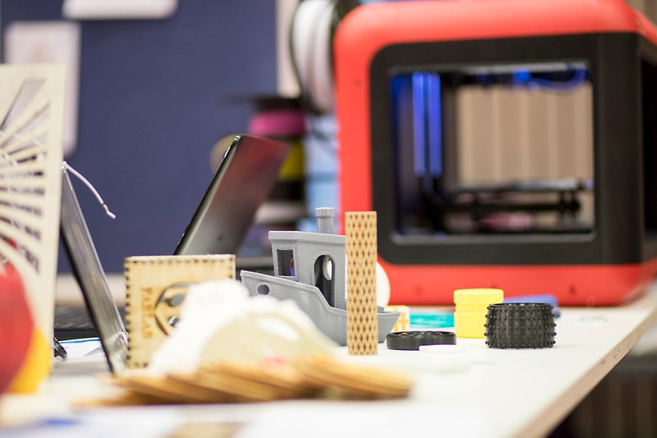 Several small objects scattered on a table in front of a 3D printer. Photo.