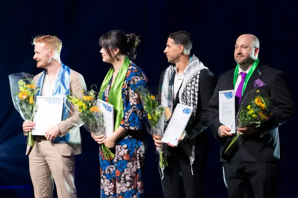 Fyra finklädda unga människor står på en scen med diplom och blommor i sina händer. Foto.