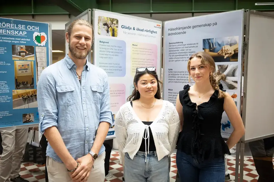 Tre studenter står framför en poster. Foto