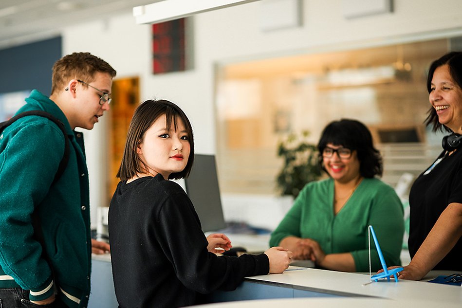 Two students standing by the reception, talking to two staff members at Halmstad University. Photo.