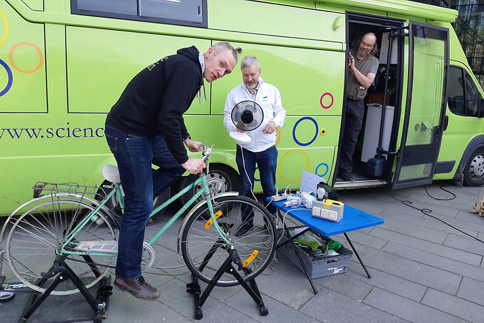 Grön minibuss parkerad, man på cykel, man som håller hårtork, man som står i bussdörren och kikar ut.