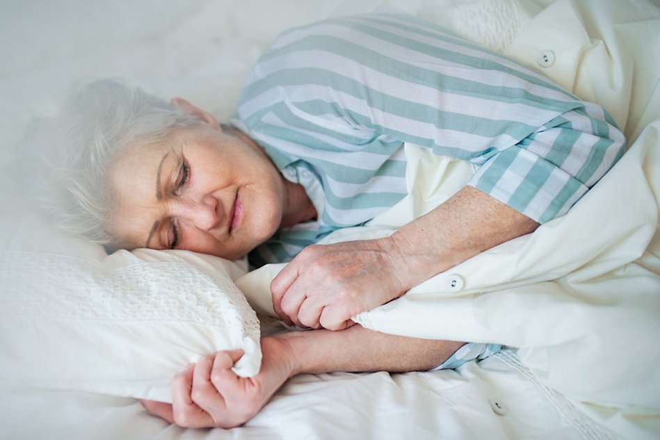 Woman with white hair sleeping on a pillow and under a duvet.