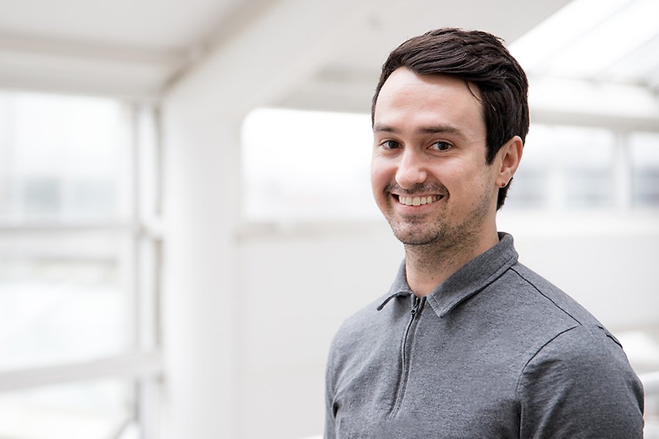 A male students smiles to the camera as he is standing in a bright white room.