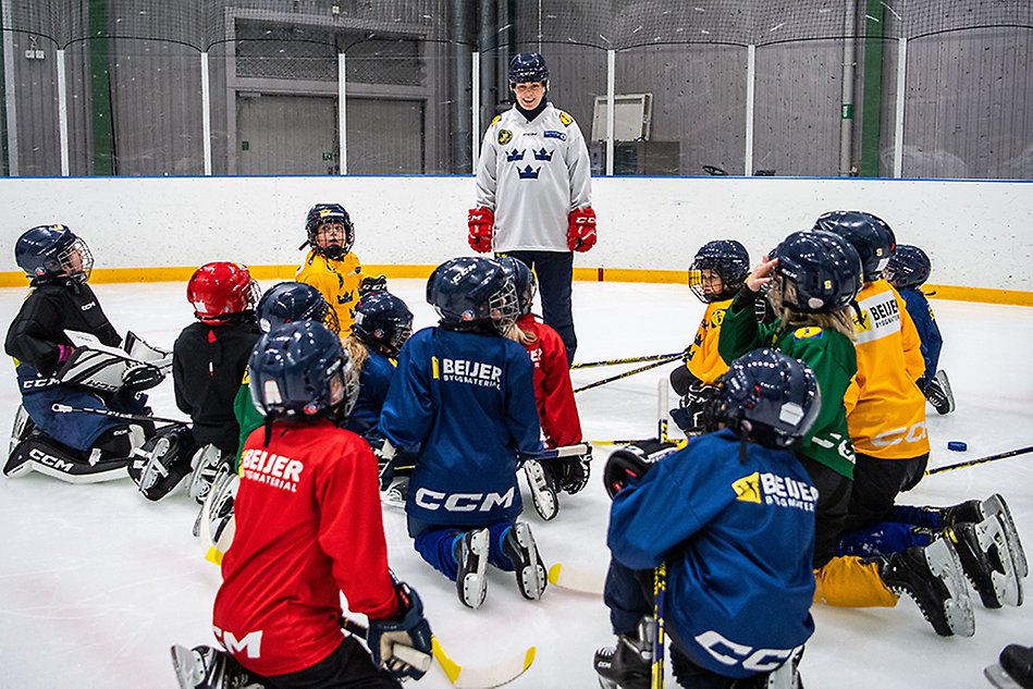 Ishockey, en tränare står framför en grupp spelare. Foto.