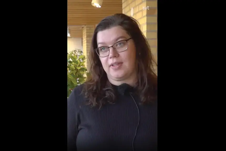 Kvinna i glasögon och brunt hår blir intervjuad.