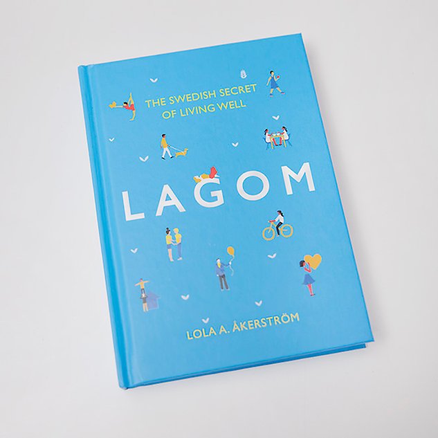 A light blue book with small figures and the text ”Lagom” lies against a white background. Photo.