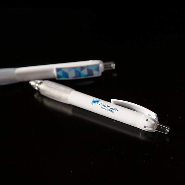 White pen with the Halmstad University logo in Swedish, seen against a black background. Photo.