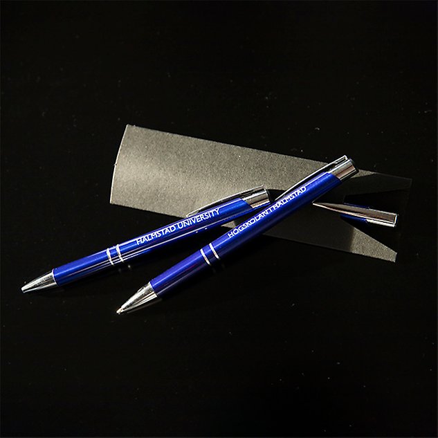 Två blå pennor i metall ligger lutade mot varandra på en svart bakgrund. Foto. 