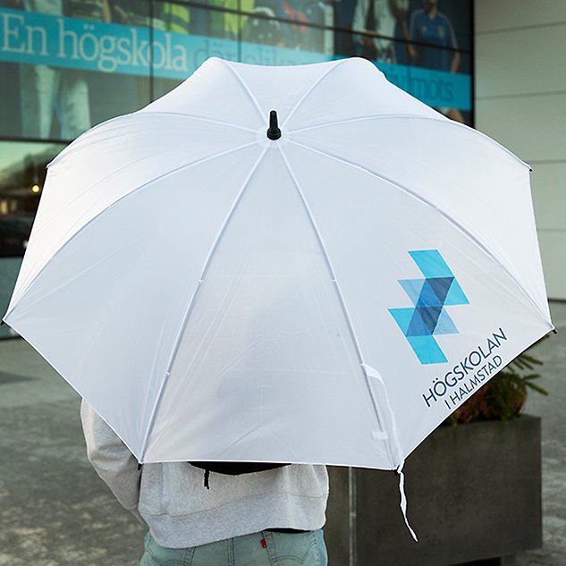 A person, seen from behind, stands under a white, unfolded umbrella. Photo.