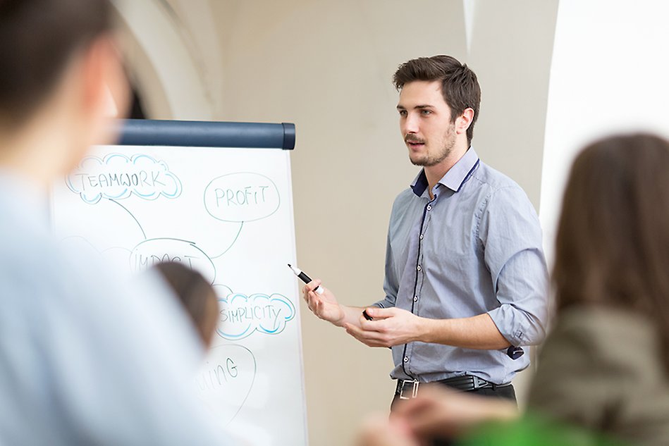 A young man stands next to a large note pad and points with a pen. Photo.