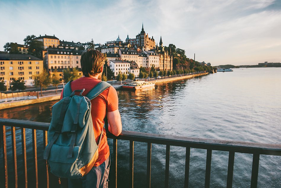 Person carrying a backpack looking out over the water, city in the background