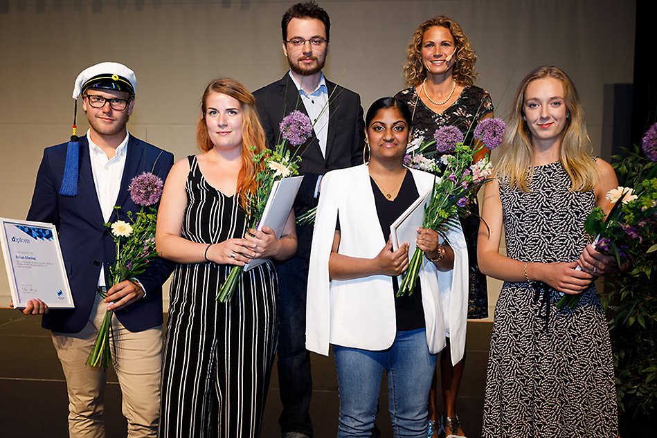 Sex finklädda personer personer står bredvid varandra, alla utom en håller var sitt diplom och blommor. Foto.