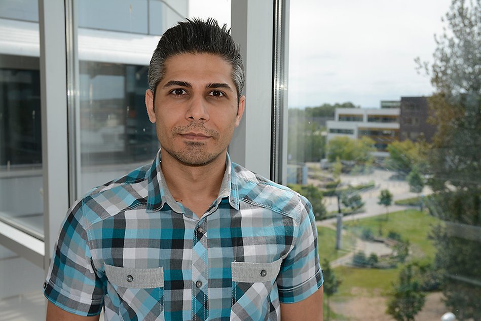Man in front of glass window with a view of the campus area. Photo.