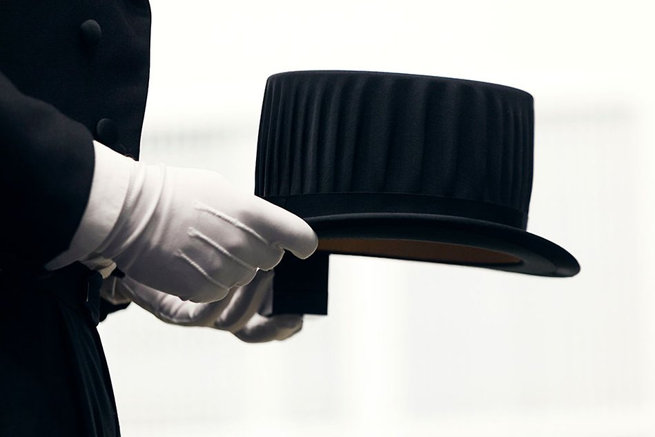 Ett par handskbeklädda händer som håller svart doktorshatt. Foto.