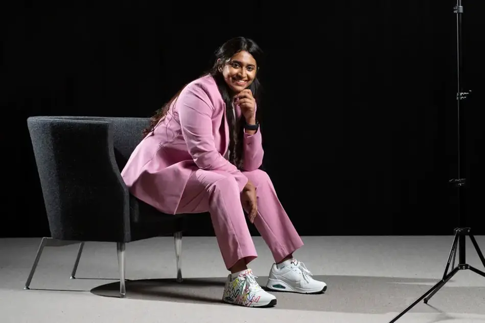 A woman in a pink suit is sitting on a chair looking into the camera. Photo.