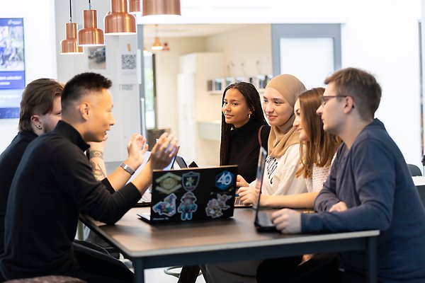 Grupp av unga personer som sitter runt ett bord och diskuterar. Foto